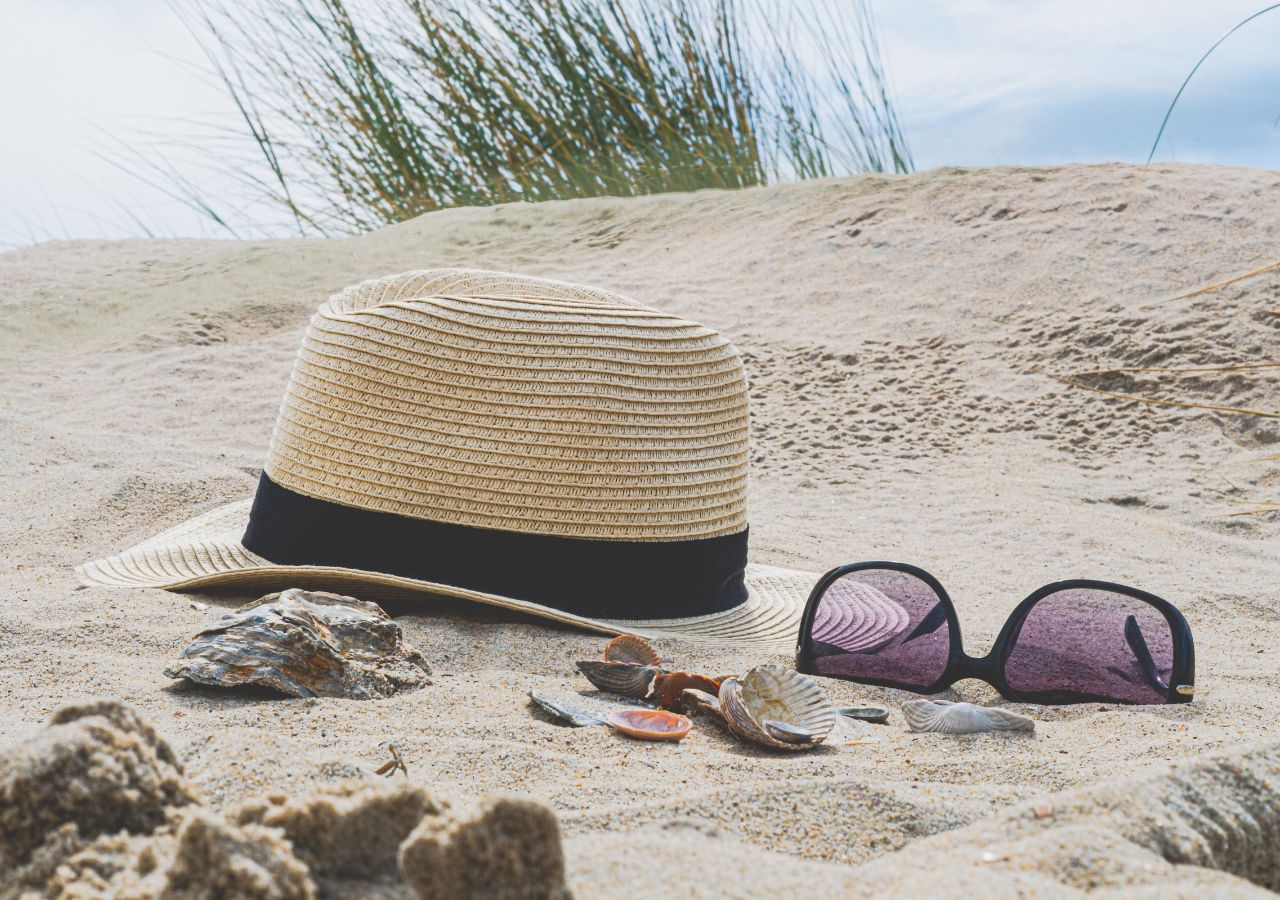 Słomkowy apelusz i okulary przeciwsłoneczne na jasnym piasku plaży