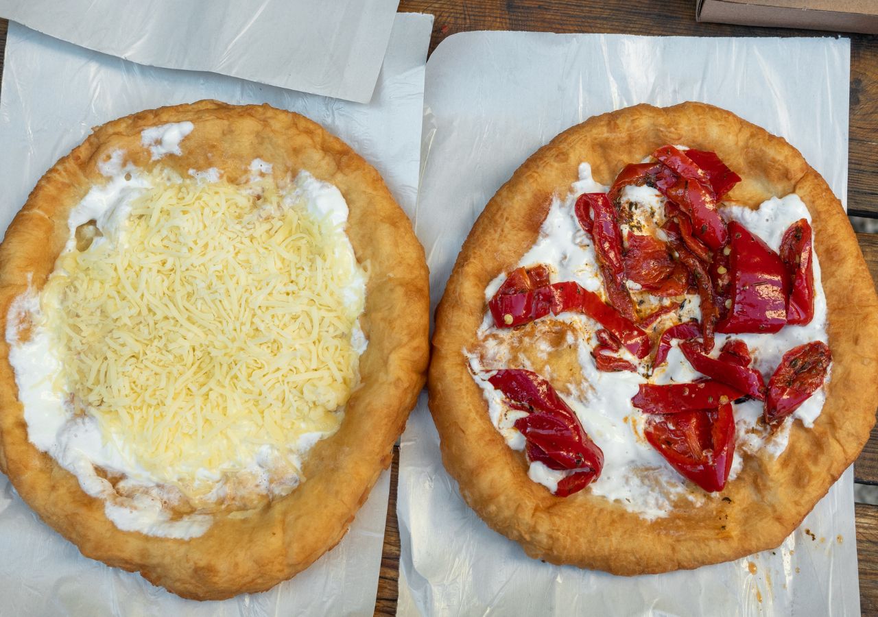 Dwa langosze węgierskie z różnymi dodatkami obok siebie na talerzu