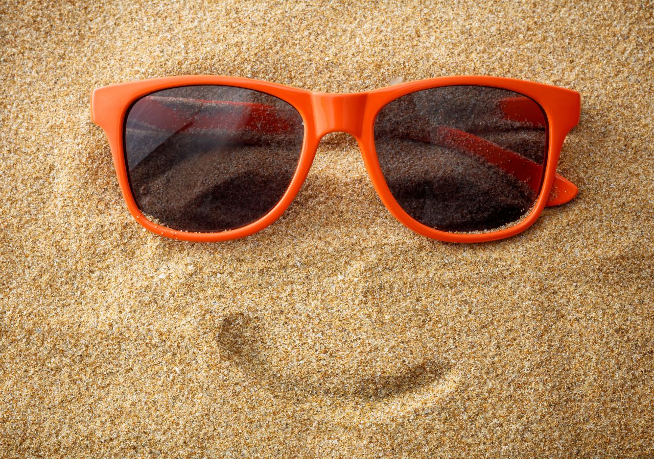 Na piasku schemat twarzy ułożony z okularów i wyrysowanego uśmiechu