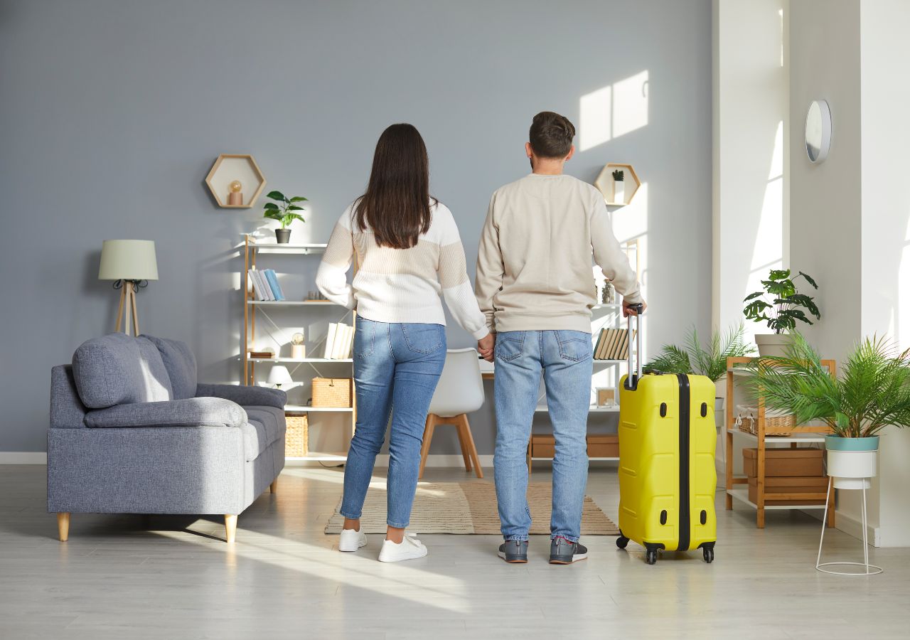 Para kobieta mężczyzna atoi tyłem w domu trzymając w ręku żółtą walizkę