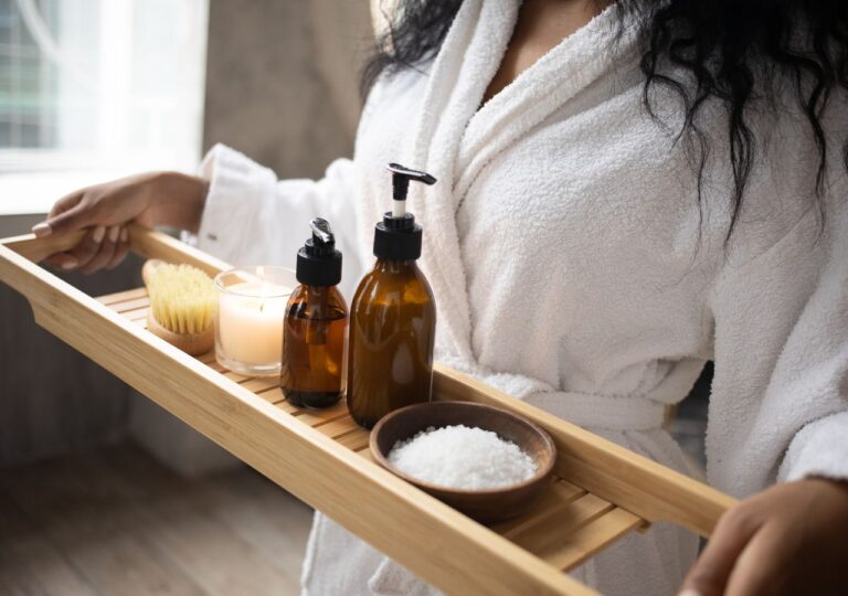 Kobieta w białym hotelowym szlafroku niesie drewnianą tacę z kosmetykami SPA