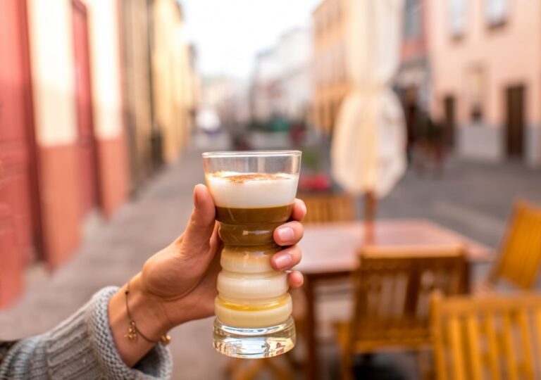 Szklanka z barraquito trzymana w ręce na kanaryjskiej ulicy